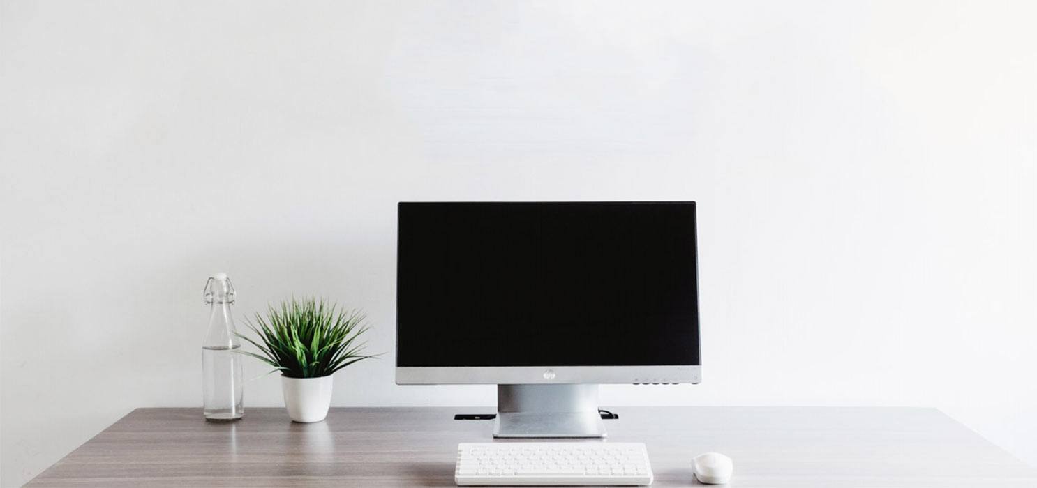 computer desk with large computer screen, plant, speaker and mouse