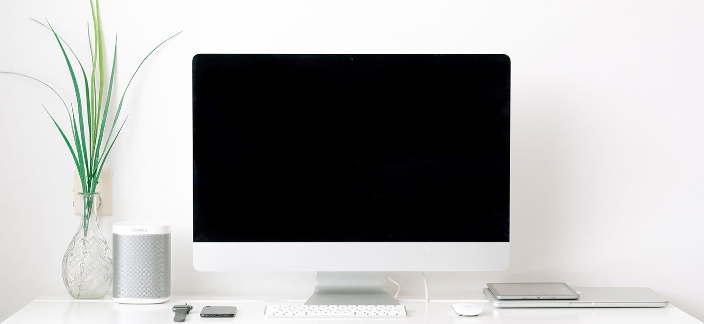 computer desk with large computer screen, plant, speaker and mouse